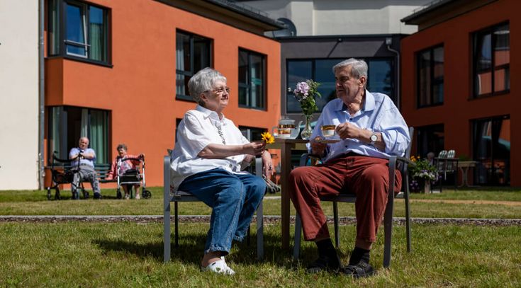 Zwei Senioren sitzen im Vorgarten der Seniorenrsidenz auf Stühlen