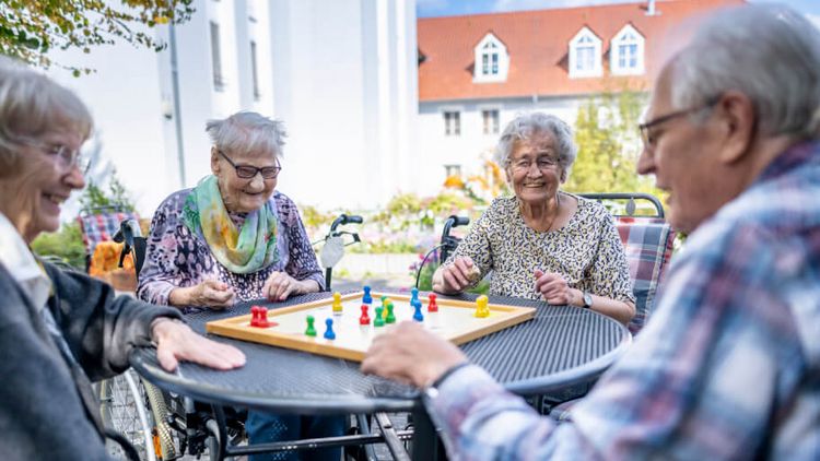 Senioren spielen draußen auf der Terrasse gemeinsam Mensch ärger dich nicht