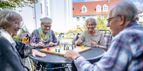 Senioren spielen draußen auf der Terrasse gemeinsam Mensch ärger dich nicht