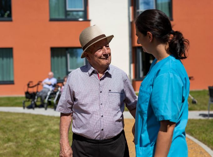 Senior und Pflegekraft unterhalten sich im Vorgarten der Seniorenresidenz