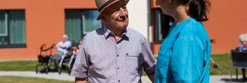 Senior und Pflegekraft unterhalten sich im Vorgarten der Seniorenresidenz