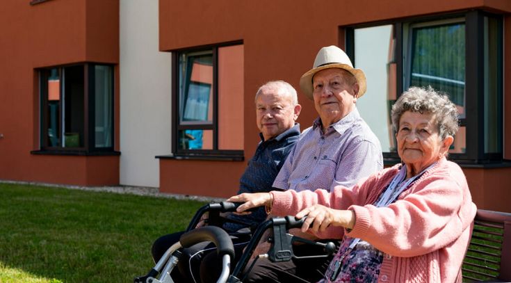 drei Senioren sitzen bei Sonnenschein im Vorgarten auf einer Bank
