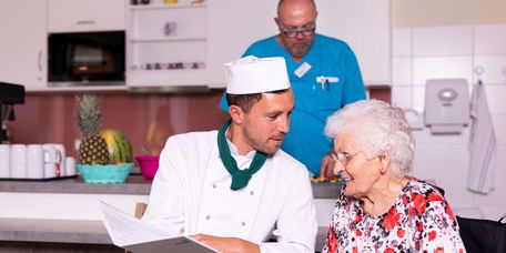 Koch mit Kochmütze serviert Seniorin Essen