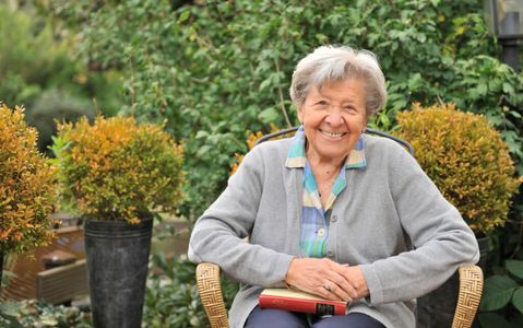 freundliche ältere Frau sitzt im Garten auf einem Stuhl