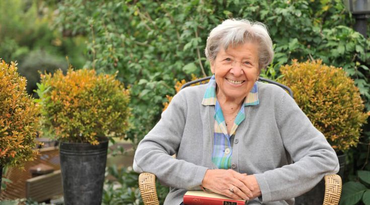 freundliche ältere Frau sitzt im Garten auf einem Stuhl