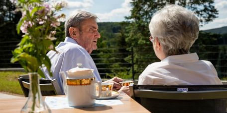 Seniorenpaar sitzt draußen am Tisch beim Kaffeetrinken