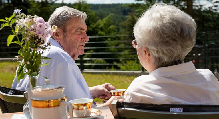 Seniorenpaar sitzt draußen am Tisch beim Kaffeetrinken