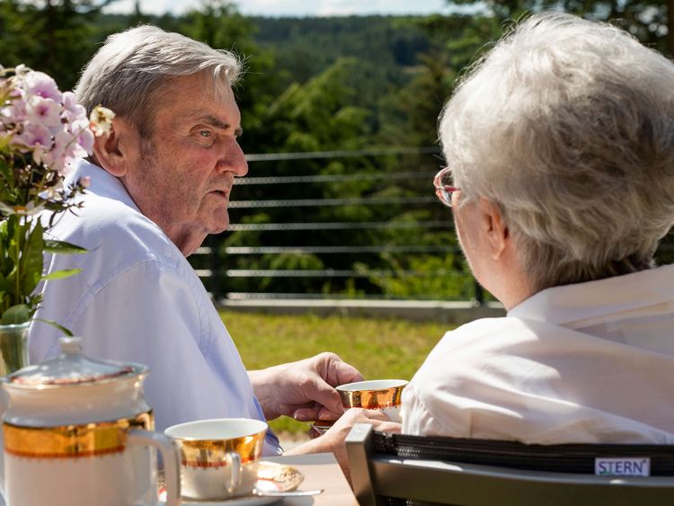 Seniorenpaar sitzt draußen am Tisch beim Kaffeetrinken
