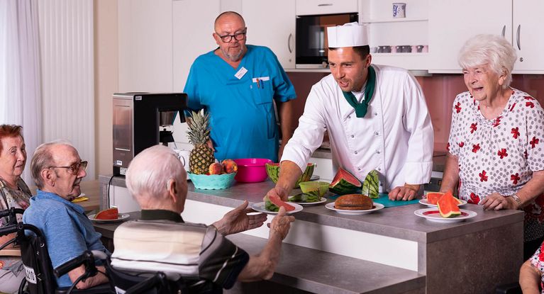 Koch mit Kochmütze serviert Senioren Essen