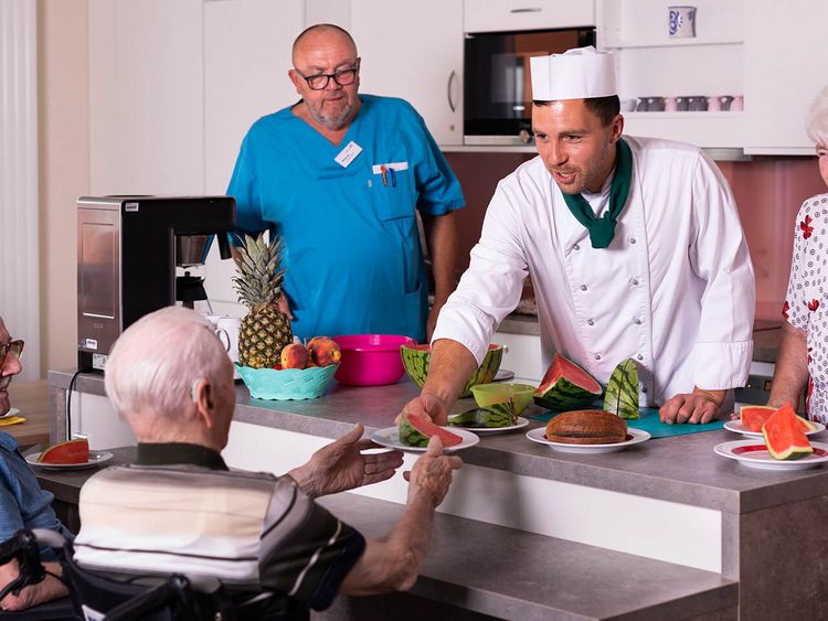 Koch mit Kochmütze serviert Senioren Essen