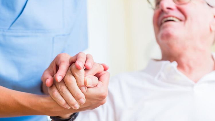 Pflegerin hält die Hand eines älteren Patienten