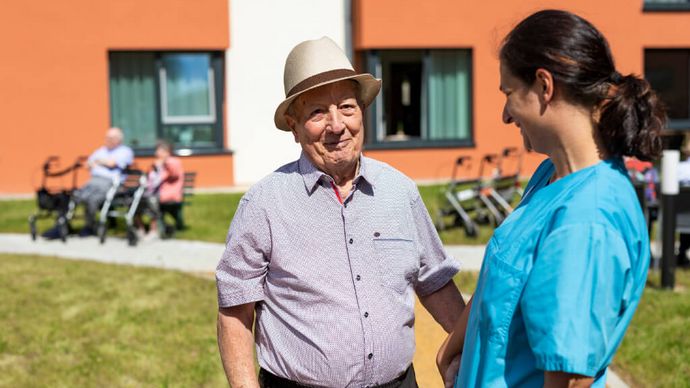 Senior und Pflegekraft unterhalten sich im Vorgarten der Seniorenresidenz