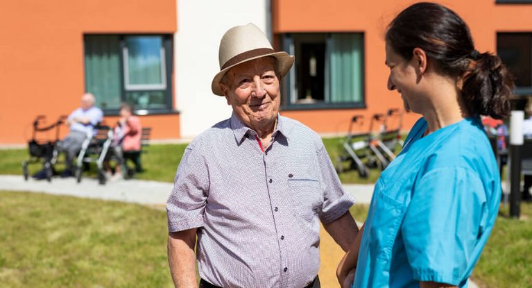 Senior und Pflegekraft unterhalten sich im Vorgarten der Seniorenresidenz