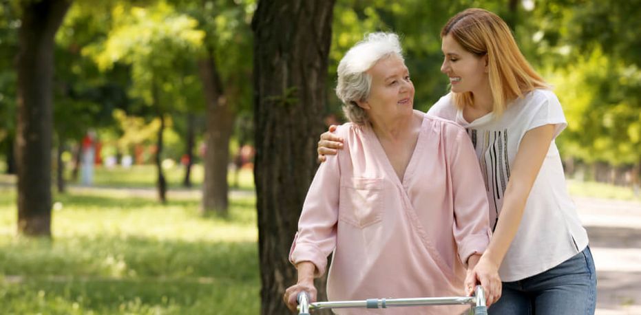 Pflegekraft und Seniorin gehen im sommerlichen Park spazieren