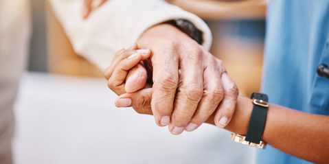 Pflegerin hält die Hand eines älteren Patienten