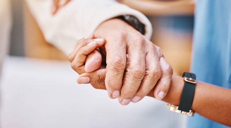 Pflegerin hält die Hand eines älteren Patienten