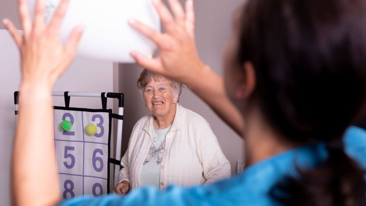 Pflegerin und Seniorin spielen Ball