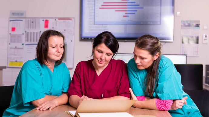 Drei weibliche Pflegekräfte besprechen die Übergabe