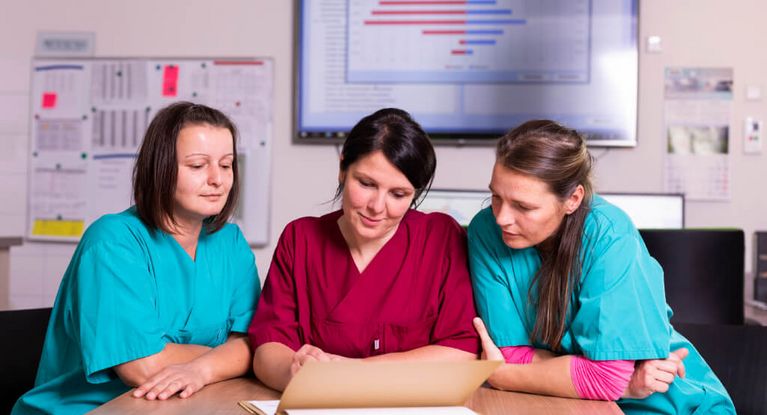 Drei weibliche Pflegekräfte besprechen die Übergabe